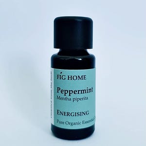 May include: A small, dark brown glass bottle with a black cap. The label is light blue and says "FIG HOME Peppermint Mentha piperita ENERGISING Pure Organic Essential Oil".