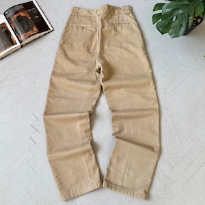 May include: Beige work trousers with a straight leg cut. The trousers have a button and zip fastening, belt loops, and two back pockets. A small brand patch is visible on the back. The trousers are laid flat on a light-coloured surface.