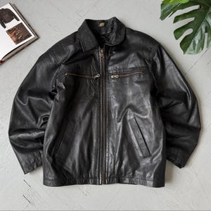 Könnte beinhalten: Eine schwarze Lederjacke mit Umlegekragen, durchgehendem Frontreißverschluss und zwei horizontalen Reißverschlusstaschen auf der Brust. Die Jacke verfügt über zwei untere vertikale Eingrifftaschen und lange Ärmel mit glatter Oberfläche.