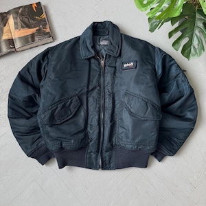May include: Dark navy blue bomber jacket with a zip-up front, two front pockets, and a ribbed hem and cuffs. The jacket features a small Schott patch on the chest. A vintage style jacket.