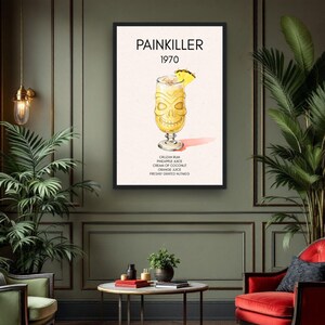 May include: A framed print featuring a cocktail illustration. The artwork displays a yellow cocktail in a tiki-style glass with a pineapple garnish. The text "PAINKILLER 1970" is at the top, with the ingredients listed below.
