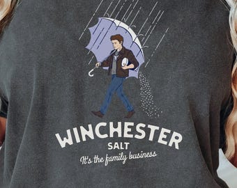 May include: Dark gray t-shirt with a graphic of a man under a purple umbrella, with salt pouring down. The text "WINCHESTER SALT" and "It's the family business" are printed below the graphic.