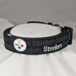 May include: Black dog collar with a repeated pattern of the word "Steelers" in gray and a Steelers logo in yellow, blue, red, and white.