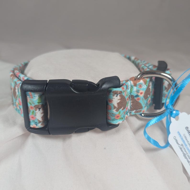 May include: A blue and brown dog print dog collar with a black plastic buckle and a silver D-ring.