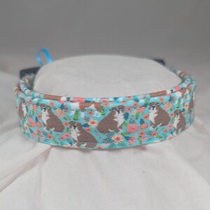 May include: A light blue dog collar with a floral pattern featuring small brown dogs and pink flowers.