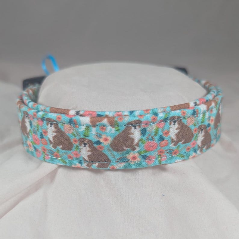 May include: A light blue dog collar with a floral pattern featuring small brown dogs and pink flowers.