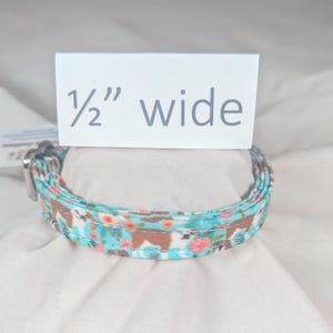 May include: A turquoise blue and brown patterned dog collar with white flowers. The collar is 1/2 inch wide.