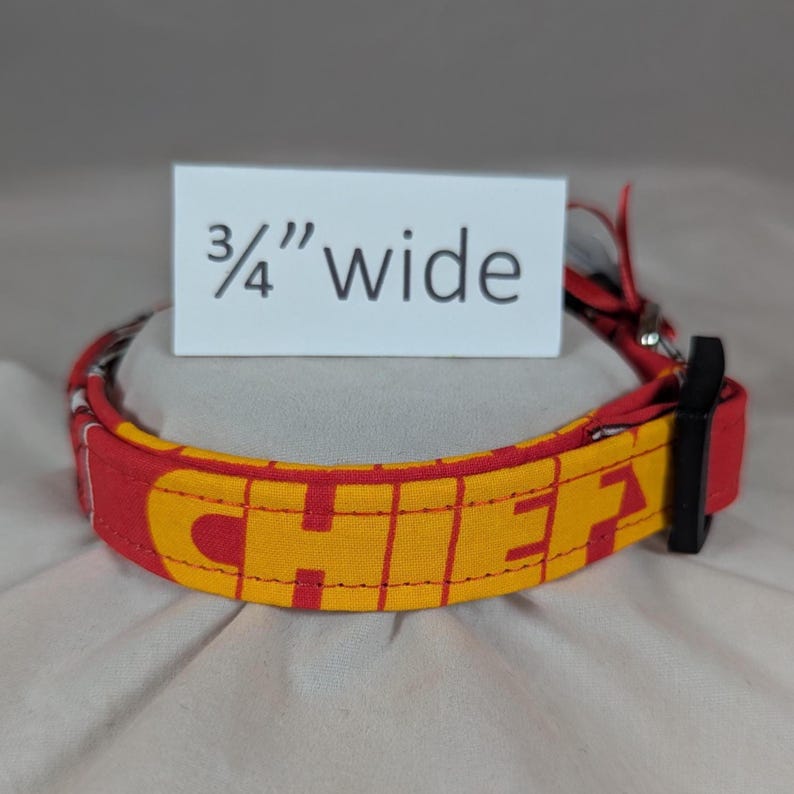 May include: A red and yellow fabric collar featuring the text CHIEFS in bold yellow lettering. A white rectangular sign positioned behind the collar displays the text 3/4" wide, indicating the width of the collar. It includes a black plastic buckle.