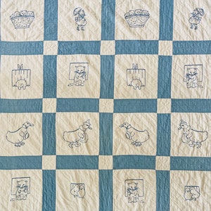 May include: A blue and white quilt with embroidered images of animals and children. The quilt is made up of squares with different images in each square. The images include a girl with an umbrella, a basket of kittens, a cat in a box, a duck with a hat, and a pair of birds.