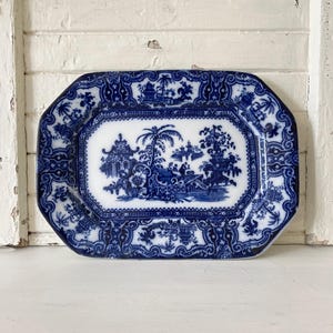 May include: A rectangular blue and white ceramic serving platter. The platter features a detailed blue transferware design with a central landscape scene surrounded by ornate borders. The design includes pagodas, trees, and figures, creating a classic aesthetic.