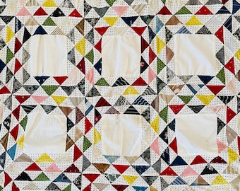 Könnte beinhalten: Ein Patchwork-Quilt mit einem sich wiederholenden Muster aus weißen Quadraten, die von bunten Dreiecken umgeben sind. Die Dreiecke sind in verschiedenen Farben gehalten, darunter Rot, Gelb, Grün und Blau, vor einem weißen, gepunkteten Hintergrund.