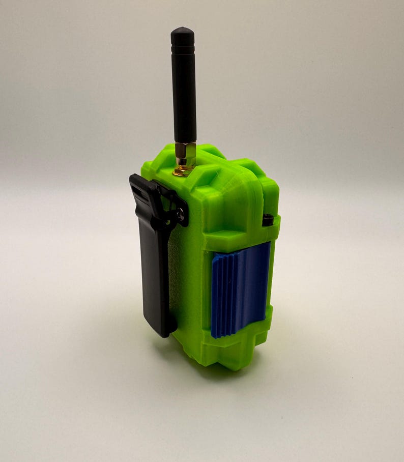 May include: A lime green electronic device with a black antenna and a black clip. The device has a blue panel on the front. The antenna is approximately 4 inches long.