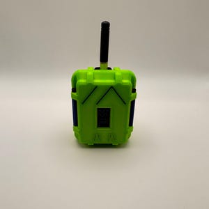 May include: A lime green electronic device with a black antenna and a small digital display. The device has blue accents and a rectangular shape with a textured surface. The device is likely a remote control or a similar electronic gadget.