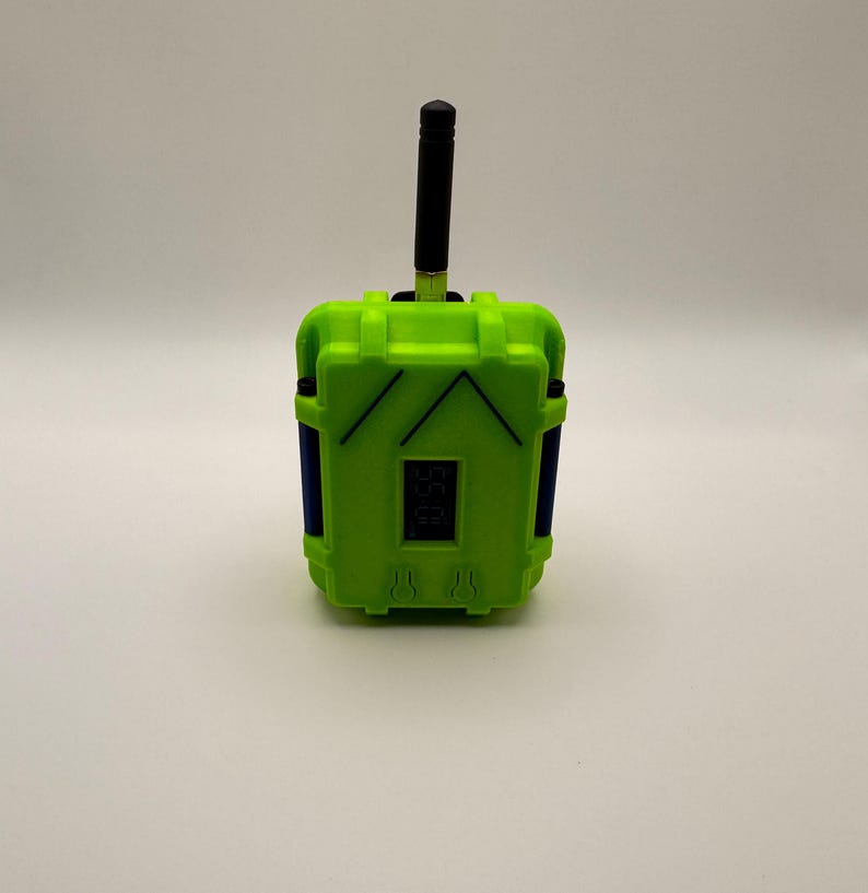 May include: A lime green electronic device with a black antenna and a small digital display. The device has blue accents and a rectangular shape with a textured surface. The device is likely a remote control or a similar electronic gadget.