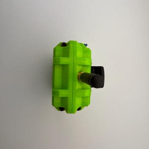 May include: A bright green rectangular device with a black cylindrical component extending from the side. The device has a textured surface and small black and blue accents. The background is a plain white wall.