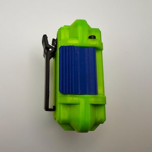 May include: A lime green rectangular device with a blue textured panel and a black clip. The device has a rounded top and bottom. The clip is attached to the side of the device.