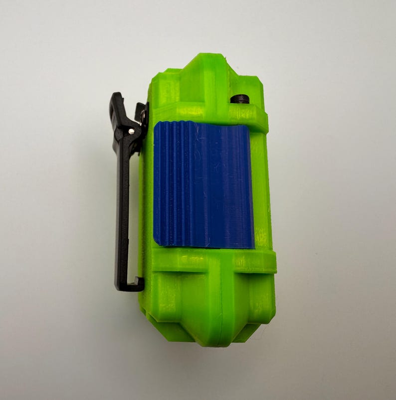 May include: A lime green rectangular device with a blue textured panel and a black clip. The device has a rounded top and bottom. The clip is attached to the side of the device.