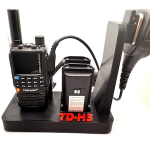 May include: Black radio communication device with a charging station. The radio has a screen and buttons. The charging station includes a microphone, two battery slots, and the text "TD-H3" in red.