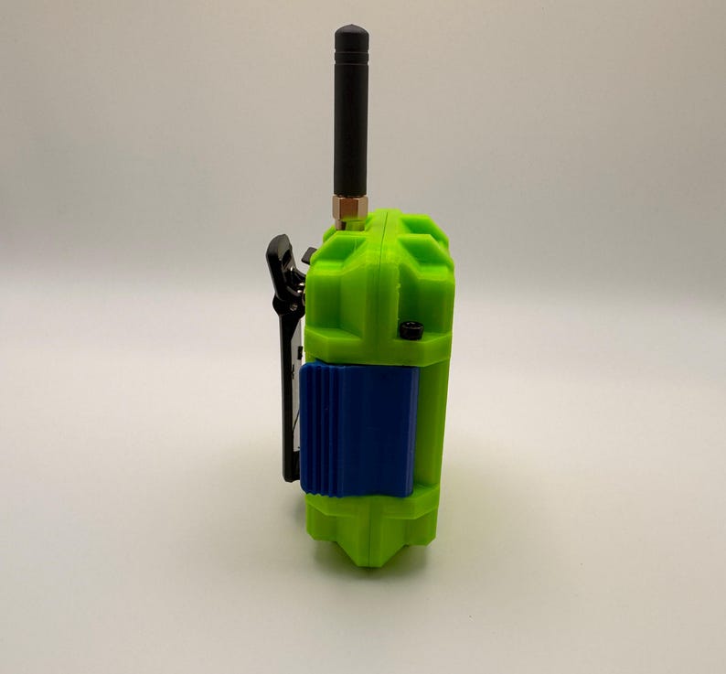 May include: A lime green walkie-talkie with a black antenna and a blue panel. The device has a black clip on the side. The antenna is approximately 4 inches long.