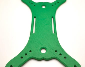 May include: Vibrant green plastic component featuring a series of holes and slots. The symmetrical design includes four extended arms, each with several small holes. A larger hole is centrally located.