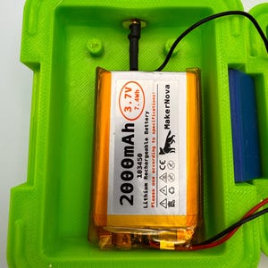 May include: A bright green rectangular enclosure with a 2000mAh Lithium Rechargeable Battery. The battery is orange and has black text that reads "MakerNova". A black antenna and wires are connected to the battery.
