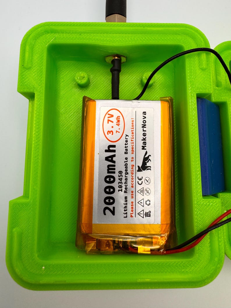 May include: A bright green rectangular enclosure with a 2000mAh Lithium Rechargeable Battery. The battery is orange and has black text that reads "MakerNova". A black antenna and wires are connected to the battery.