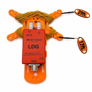 Peut inclure: Un enrouleur d'antenne en plastique orange contient du fil jaune, avec un boîtier rouge LDG RU-9:1 Unun doté de deux bornes argentées et d'un connecteur coaxial. Deux étiquettes orange marquées 29ft. et 17ft. sont fixées aux extrémités du fil.