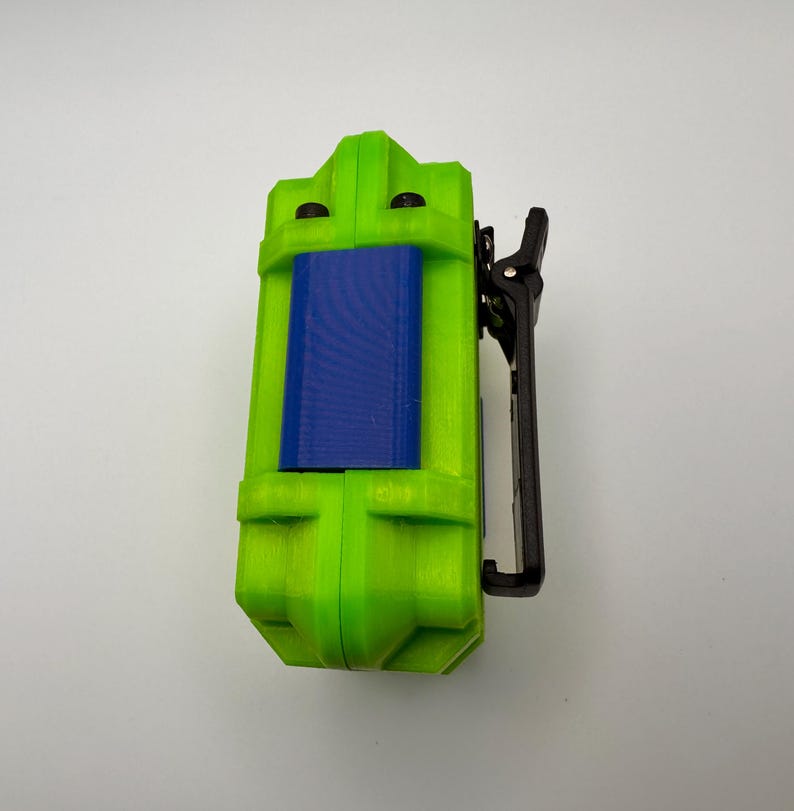 May include: A lime green rectangular device with a blue center panel and a black clip. The device has a textured surface and a geometric design. The clip is attached to the side of the device.