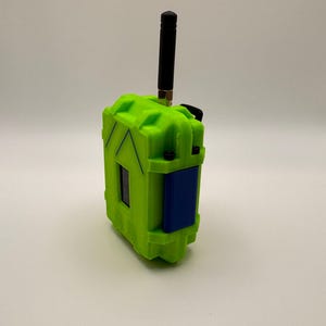 May include: A neon green rectangular device with a black antenna and a blue panel. The device has a textured surface and appears to be made of plastic. The antenna is black and extends upwards from the top of the device.