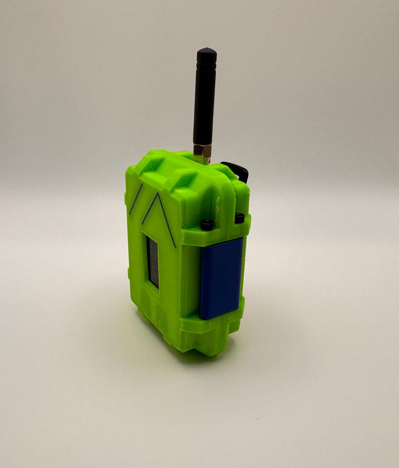 May include: A neon green rectangular device with a black antenna and a blue panel. The device has a textured surface and appears to be made of plastic. The antenna is black and extends upwards from the top of the device.