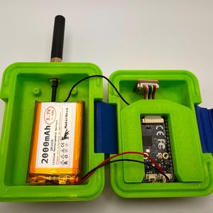 May include: Open green plastic case with a black antenna, a 2000mAh battery, and a circuit board. The case is open, revealing the internal components. The battery is labeled "MakerNova" and "3.7V". Wires connect the components.