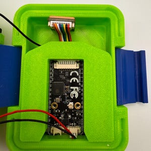 May include: A green 3D-printed enclosure with a black circuit board inside. The board has multiple connectors and is connected to colored wires. The enclosure has blue and green components and the text "HTIT-HB32LAF V4.2" and "CE FC".