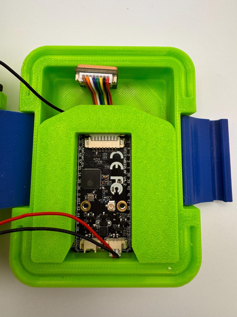 May include: A green 3D-printed enclosure with a black circuit board inside. The board has multiple connectors and is connected to colored wires. The enclosure has blue and green components and the text "HTIT-HB32LAF V4.2" and "CE FC".