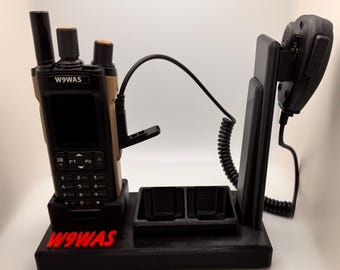 May include: Black radio communication device with a charging station. The radio is black and tan with a keypad and antenna. The charging station has two charging slots and a holder for a microphone. The text "W9WAS" is in red.
