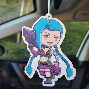 May include: A blue-haired cartoon character with a pink and black outfit and a rocket launcher. The character is holding a rocket launcher and has a blue braid. The character is a car air freshener.