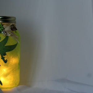 May include: A green glass jar with a fairy silhouette and a green flower on the lid. The jar is lit from inside, creating a warm glow.