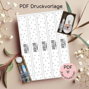 Puede incluir: Un PDF imprimible con temática de cumpleaños. El diseño presenta un fondo blanco con lunares negros y las palabras "Happy Birthday". Dos pequeñas cajas de madera contienen velas y objetos decorativos. También es visible el texto "PDF Zum Download".