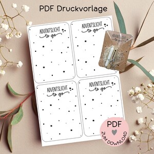 Può includere: Un foglio di quattro etichette rettangolari bianche con angoli arrotondati, ognuna con il testo "ADVENTSLICHT to go" e forme di stelle nere sparse. È visibile un piccolo pacchetto con candele e spago. L'immagine include anche il testo "PDF Druckvorlage" e un cerchio rosa con "PDF" e "Zum Download".