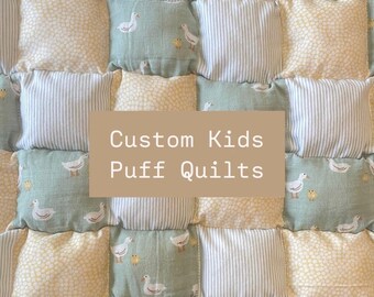 May include: A custom kids puff quilt with a patchwork design featuring yellow, white, and green squares with duck and chick patterns. The quilt has the text "Custom Kids Puff Quilts" in the center.