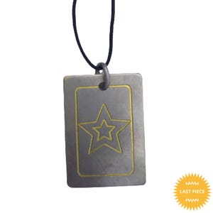 May include: A rectangular pendant with a star design, suspended from a black cord. The pendant is a muted grey colour with a gold-coloured star outline. The words "LAST PIECE" are on a yellow sticker.