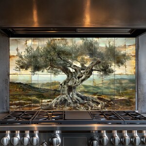 Puede incluir: Un protector contra salpicaduras de cocina con una pintura detallada de un olivo antiguo. La obra de arte muestra un tronco y ramas extensas, sobre un fondo de colinas y un cielo nublado, creando una escena rústica y natural.