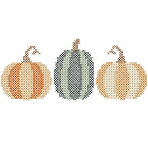 May include: A cross-stitch pattern featuring three pumpkins arranged in a row. The left and right pumpkins are orange and cream with brown stems, while the center pumpkin is sage green and dark gray with a brown stem, all rendered in a grid.