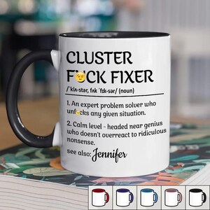 May include: White ceramic mug with a black handle and rim. The mug features the text "CLUSTER FOCK FIXER" with a definition and the name "Jennifer". The mug is on a floral patterned surface.