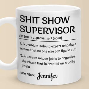 Puede incluir: Taza de cerámica blanca con el texto "SHIT SHOW SUPERVISOR" en negro. La taza incluye una definición del término y el nombre "Jennifer" en la parte inferior. Una idea de regalo humorística.