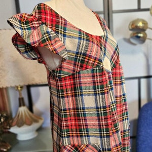 May include: A red, white and blue plaid dress with a ruffled neckline and short sleeves. The dress has a patch pocket on the front.