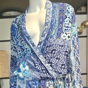 May include: A blue and white patterned wrap dress with long sleeves and a ruffled hem. The dress features a variety of blue patterns and designs. The dress is displayed on a mannequin.