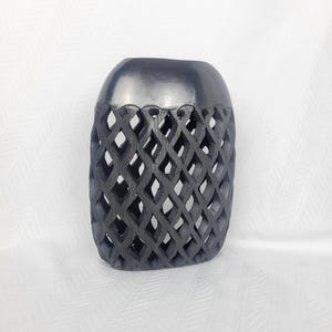 May include: A dark grey, hand-carved wooden vase with a geometric diamond pattern. The vase has a smooth, rounded top and a cylindrical body with openwork diamond shapes. The vase is a decorative item.