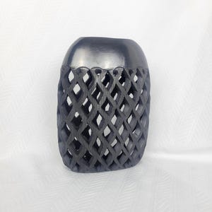 May include: A matte black cylindrical vase featuring a solid smooth top section and a lower body characterized by an intricate, open-work diamond lattice pattern. The structure is uniform in color and displays a consistent geometric design.