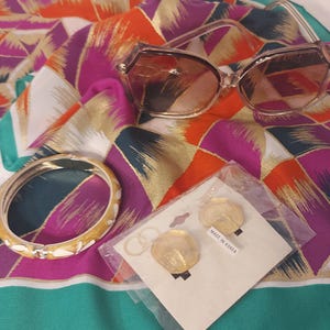May include: A colorful patterned scarf with a pair of brown sunglasses, a gold bangle bracelet, and a pair of gold hoop earrings. The earrings are packaged in a clear plastic bag with a white label that says "Made in Korea".