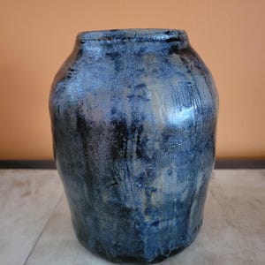 May include: A handmade ceramic vase with a dark blue and black glaze. The vase has a rounded body and a slightly flared rim. The surface has a textured appearance with streaks of lighter blue and gold.
